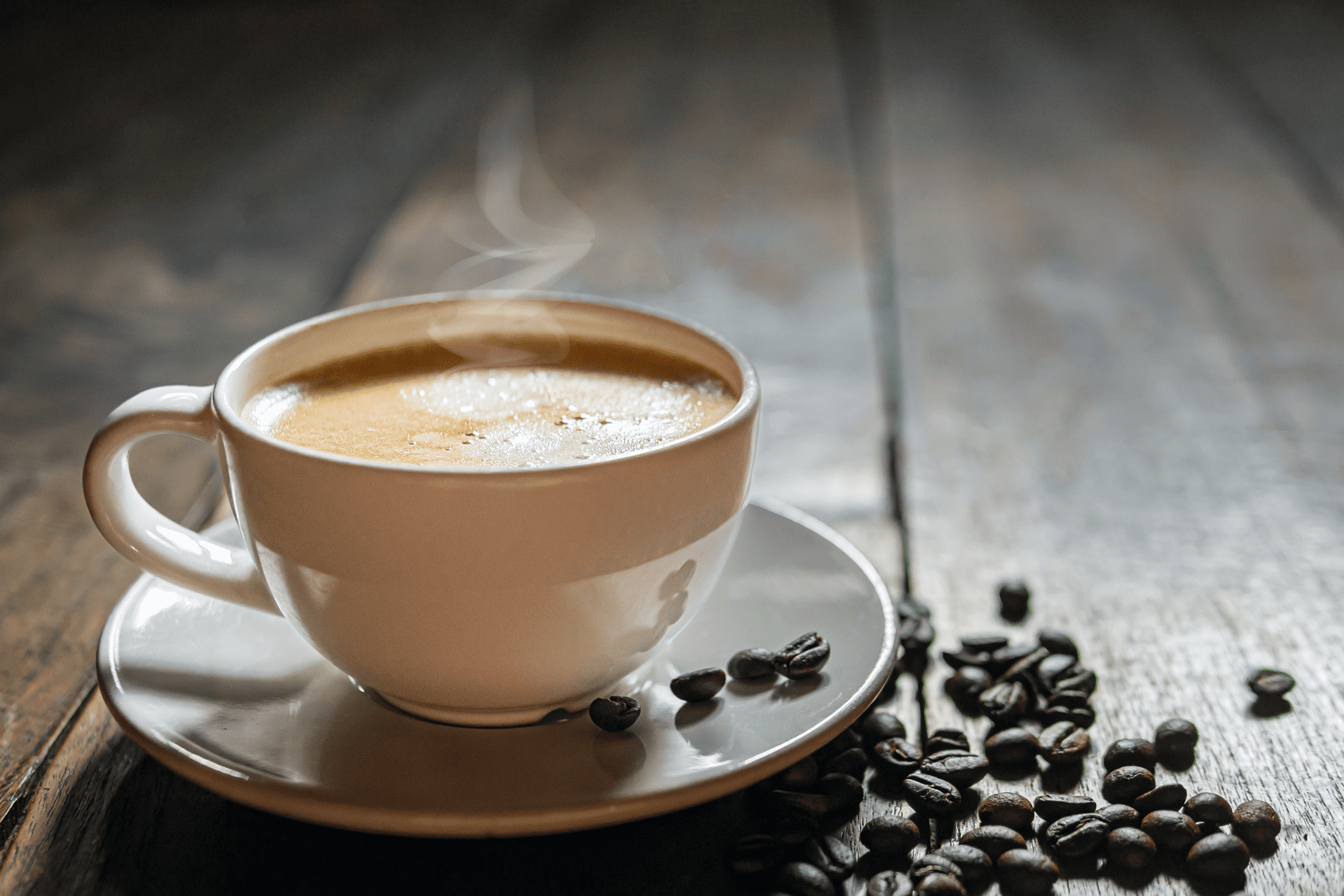 Steaming cup of coffee with scattered coffee beans on a rustic wooden surface.