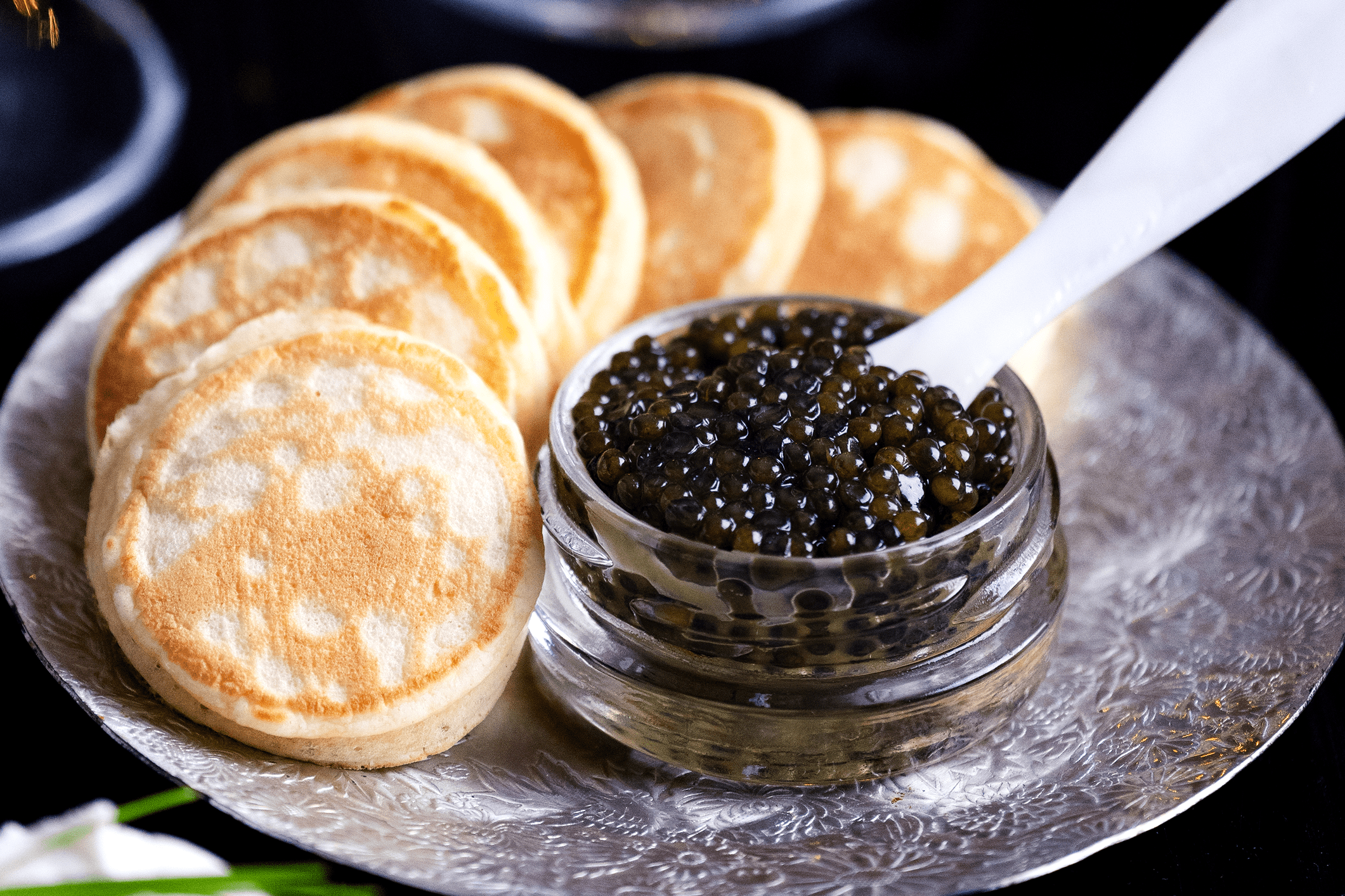 Jar of black caviar with blinis on a silver platter.